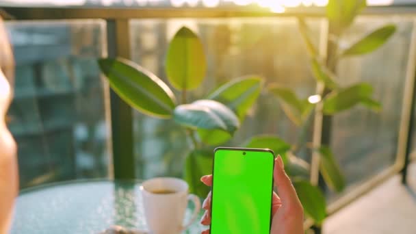 Frau sitzt in einem Café und benutzt Smartphone mit grünem Bildschirm im vertikalen Modus. Mädchen surfen im Internet, schauen Inhalte, Videos, Blogs. — Stockvideo