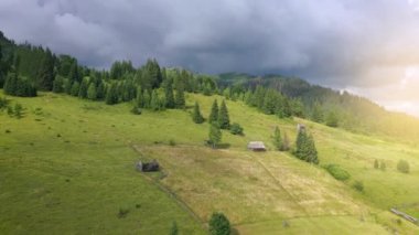 Güzel mistik bir dağ manzarası üzerinde uçmak. Kozalaklı orman, dağlar, fırtına bulutları, küçük ahşap evler.