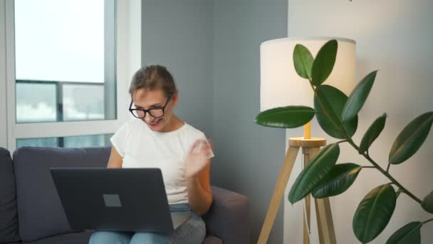 Casual klädd kvinna med glasögon sitter på soffan och kommunicerar via videolänk med familj eller nära vänner — Stockvideo