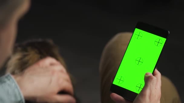 Man using smartphone with green mock-up screen in vertical mode and stroking cat. Man browsing Internet, watching content, videos. — Vídeo de stock