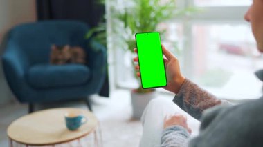 Evde dikey modda yeşil ekranlı akıllı telefon kullanan bir kadın var. Kız internette geziniyor, içeriği izliyor, videolar
