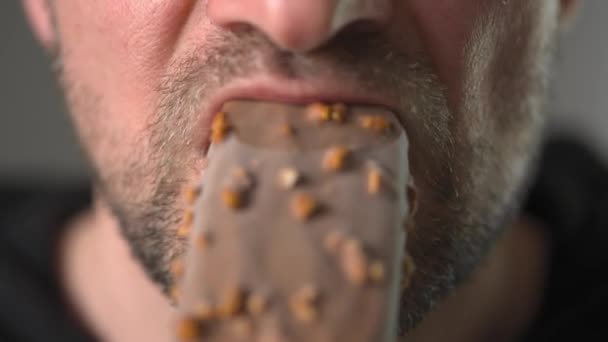 Man enjoying eating chocolate covered ice cream with nuts — Stock video