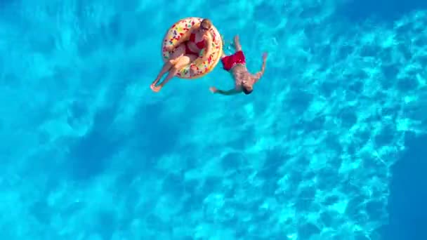 Vista aérea de um casal se divertindo na piscina, o homem nada e a mulher está em um donut inflável — Vídeo de Stock