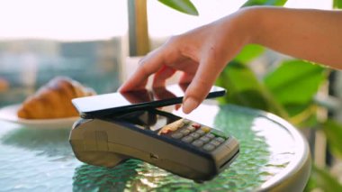Akıllı telefondan yapılan temassız ödeme. Kablosuz ödeme konsepti. Yakın plan, kadın bir kafedeki banka terminalinin siparişini ödemek için akıllı telefon nakitsiz cüzdan teknolojisi kullanıyor..
