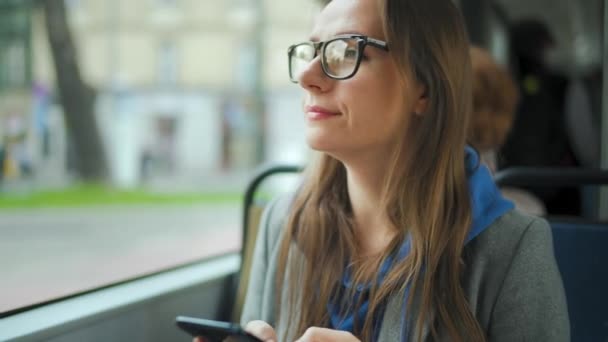Frau mit Brille in Straßenbahn mit Smartphone im Chat und SMS mit Freunden. Stadt, Stadt, Verkehr. — Stockvideo