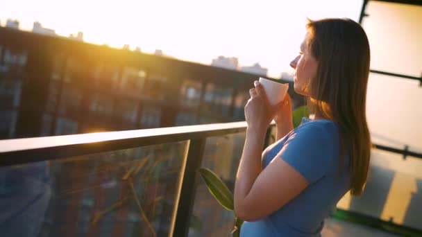 Kobieta pijąca kawę lub herbatę stojąc na balkonie i podziwiając zachód słońca. — Wideo stockowe