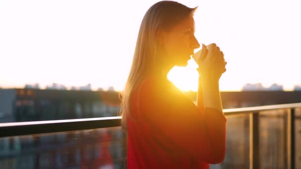 Woman drinking coffee while standing on the balcony and admire the sunset. — Stok Video