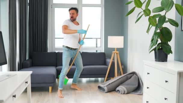 Hombre limpiando la casa y divirtiéndose bailando con una escoba. Movimiento lento — Vídeo de stock