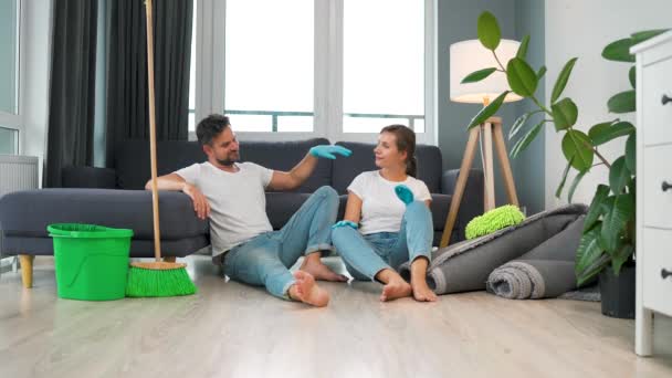 Casal cansado senta-se no chão em uma sala e alta cinco uns aos outros depois que eles terminam de limpar a casa. Movimento lento — Vídeo de Stock