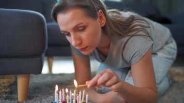 Doğum günü pastasında mum yakan bir kadın, evde yalnız başına doğum gününü kutluyor.
