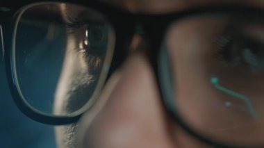 Gözlüklü kadın monitöre bakıyor ve çizelgeler ve analizlerle çalışıyor. Monitör ekranı gözlüklere yansıyor. Gece çalış. Aşırı yakın çekim