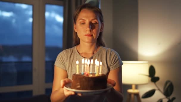 Счастливая взволнованная женщина загадывает заветное желание и раздувает свечи на праздничном торте, празднуя день рождения дома, замедляет ход — стоковое видео
