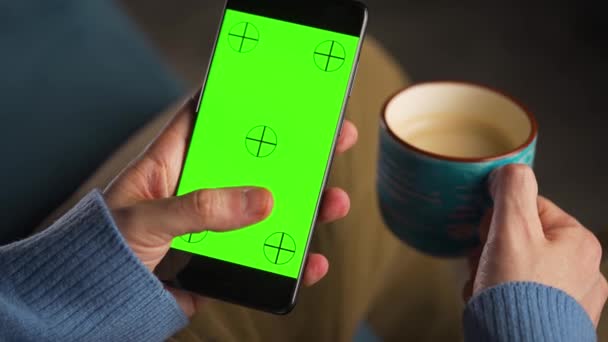 Man met smartphone met groene mock-up scherm in verticale modus en het drinken van koffie. Man surfen op internet, kijken naar inhoud, video 's. — Stockvideo