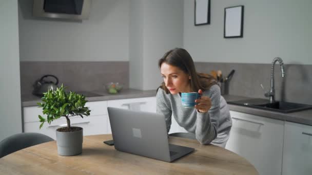 Donna con una tazza di caffè in mano in piedi in casa accogliente uso cucina portatile fare lavoro freelance, chattare con qualcuno, rispondere alle e-mail. Concetto di lavoro a distanza. — Video Stock