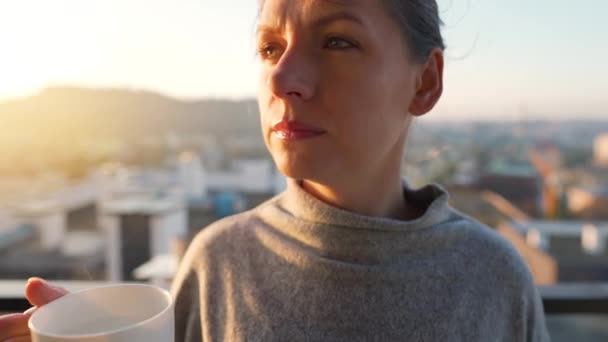 Femme commence sa journée avec une tasse de thé ou de café et vérifier les e-mails dans son smartphone sur le balcon à l'aube. — Video