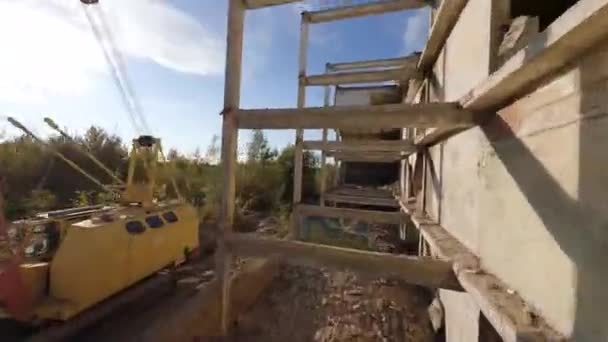 Dron FPV płynnie lata wśród opuszczonych budynków przemysłowych i wokół koparki. — Wideo stockowe
