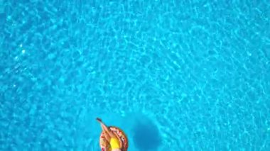 Havuzda donutun üzerinde yatan sarı mayo giymiş bir kadının hava manzarası.