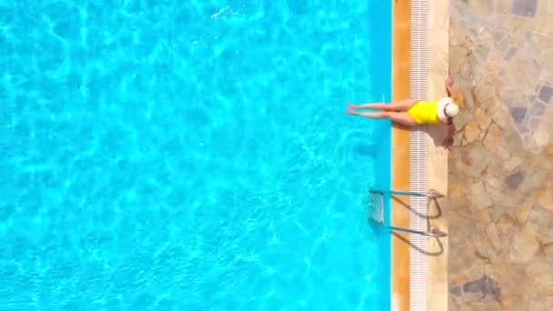 Letecký pohled na ženu ve žlutých plavkách a klobouku sedí na okraji bazénu — Stock video