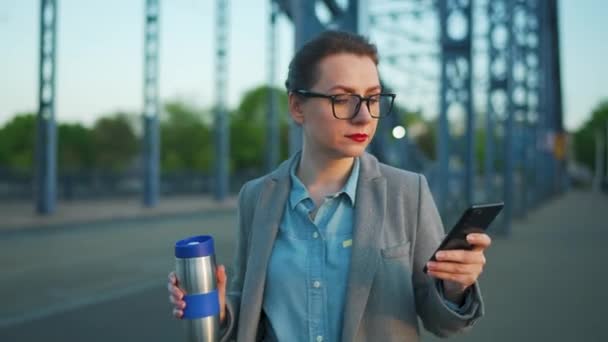 Mujer con abrigo, paseando por la ciudad por la mañana temprano, tomando café y usando smartphone. Comunicación, día de trabajo, concepto de vida ocupada. — Vídeos de Stock
