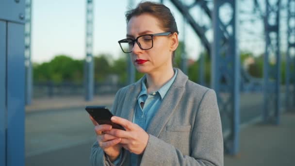 Femme en manteau se promener dans la ville tôt le matin et en utilisant smartphone.. Communication, journée de travail, concept de vie occupée. — Video