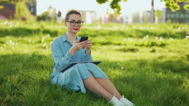 Mujer usando teléfono inteligente mientras está sentado en el parque después de terminar el trabajo al aire libre al atardecer — Vídeos de Stock