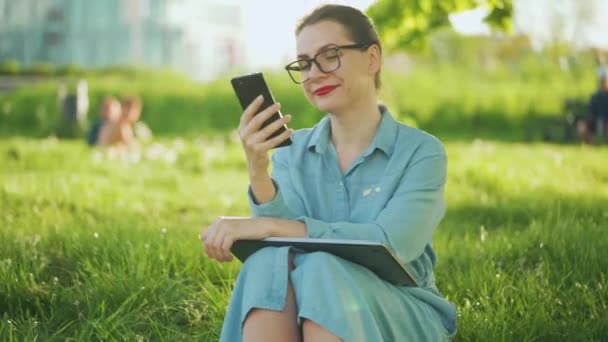 Kvinna som använder smartphone när du sitter i parken efter att ha avslutat utomhus arbete vid solnedgången — Stockvideo