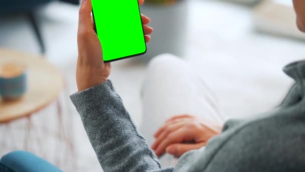 Frau zu Hause mit Smartphone-Attrappe mit grünem Bildschirm im vertikalen Modus. Mädchen surfen im Internet, schauen Inhalte, Videos — Stockvideo