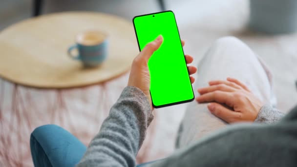 Женщина дома использует смартфон с зеленым макетом экрана в вертикальном режиме. Девушка просматривает Интернет, смотрит контент, видео. POV. — стоковое видео