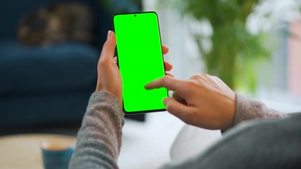 Kvinna hemma med hjälp av smartphone med grön mock-up skärm i vertikalt läge. Flicka surfa på Internet, titta på innehåll, videor. Födelsedatum. — Stockvideo