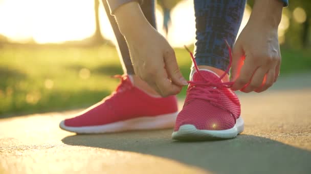 Woman tying shoelaces while jogging or walking at sunset — Stock Video