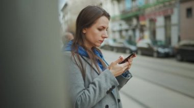 Palto giymiş bir kadın sokakta dikiliyor ve akıllı telefon kullanıyor iletişim, iş günü, yoğun yaşam konsepti..