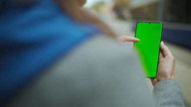 Sokaktaki kadın, geçen bir tramvayın arka planına dikey modda yeşil ekran kullanan akıllı telefon kullanıyor.