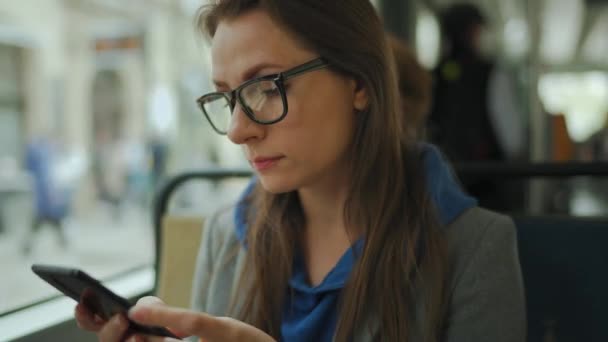 Mujer con gafas en tranvía utilizando el chat de teléfonos inteligentes y mensajes de texto con amigos. Ciudad, urbano, transporte. — Vídeos de Stock