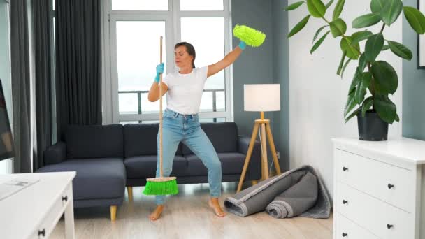 Donna in cuffia pulire la casa e divertirsi ballando con una scopa e un panno. Rallentatore — Video Stock