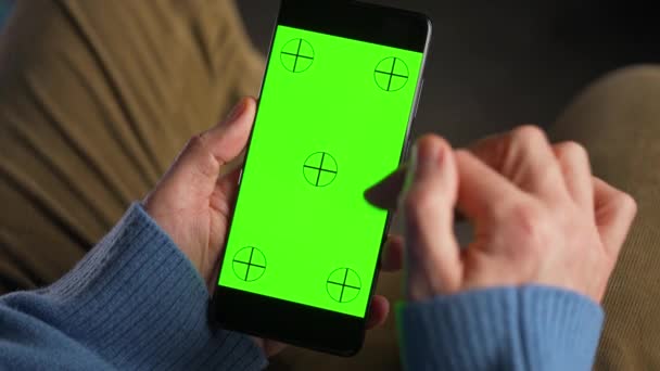 Man using smartphone with green mock-up screen in vertical mode. 인터넷 검색, 콘텐츠보기, 비디오보기. — 비디오