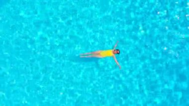 Sarı mayolu bir kadının havuzda sırtüstü yatışı. Rahatlatıcı konsept, yaz yaşam tarzı