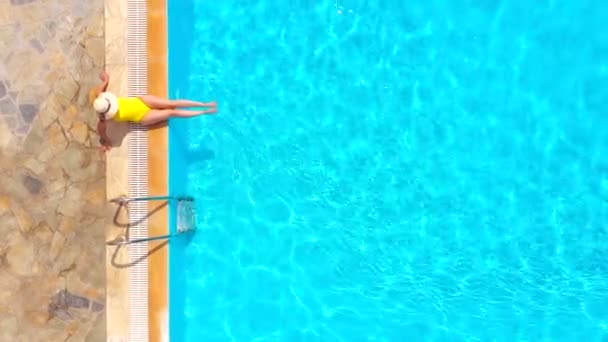 黄色の水着を着た女性のトップダウンビューと帽子はプールの端に座っています 夏のライフスタイル 休息とリラクゼーションの概念 — ストック動画