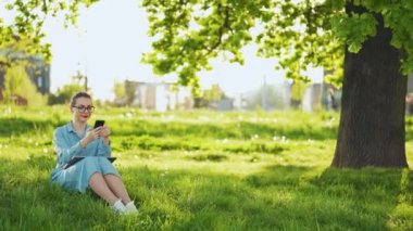 Gün batımında açık havada işi bittikten sonra parkta otururken akıllı telefon kullanan bir kadın. Dışarıda çalışan serbest çalışan biri.