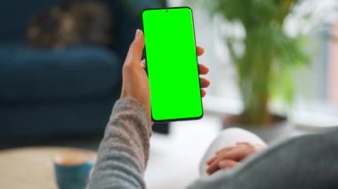 Evde dikey modda yeşil ekranlı akıllı telefon kullanan bir kadın var. İnternette gezinen, içerik izleyen, videolar, bloglar. POV.