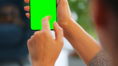 Evde dikey modda yeşil ekranlı akıllı telefon kullanan bir kadın var. Kız internette geziniyor, içeriği, videoları, blogları izliyor.