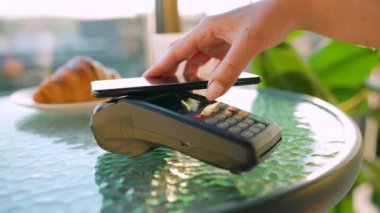 Cep telefonu ödemesi. Akıllı telefondan yapılan temassız ödeme. Kablosuz ödeme konsepti. Yakın plan, kadın bir kafedeki banka terminalinin siparişini ödemek için akıllı telefon nakitsiz cüzdan teknolojisi kullanıyor..