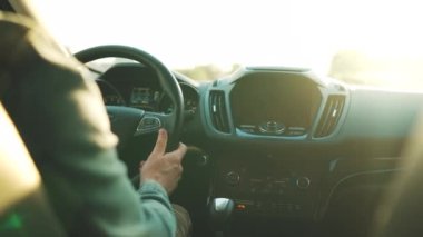 Adam yol boyunca araba sürüyor, batan güneş ön camda parlıyor. Sürücülerin omzunun arkasından bak.