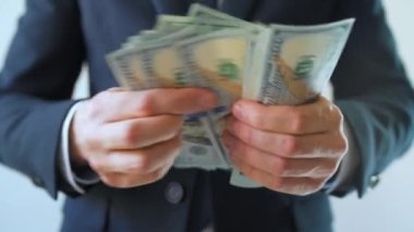 Resmi olarak giyinmiş bir adam Amerikan dolarlarını sayıyor, yakın plan. Yatırım, başarı, finansal beklentiler veya kariyer ilerlemesi kavramı