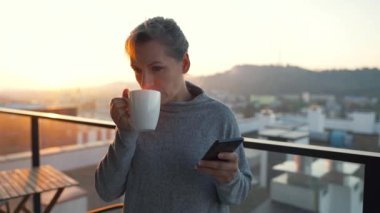 Kadın güne bir fincan çay ya da kahveyle başlıyor ve şafak vakti balkondaki akıllı telefonundaki e-postaları kontrol ediyor, ağır çekimde. Modern şehir yaşam tarzı