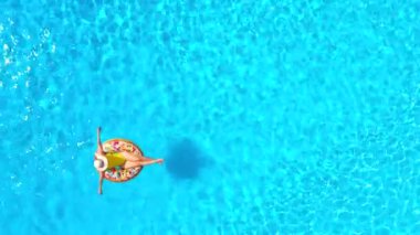 Havuzdaki bir çöreğin üzerinde sarı mayo giymiş bir kadının havadan görünüşü. Yaz yaşam tarzı, dinlenme ve rahatlama kavramı