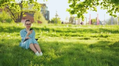 Gün batımında açık havada işi bittikten sonra parkta otururken akıllı telefon kullanan bir kadın. Dışarıda çalışan serbest çalışan biri.