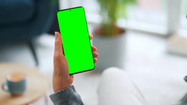 Evde dikey modda yeşil ekranlı akıllı telefon kullanan bir kadın var. Kız internette geziniyor, içeriği, videoları, blogları izliyor.