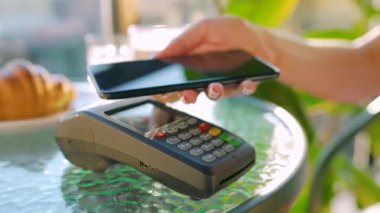 Cep telefonu ödemesi. Akıllı telefondan yapılan temassız ödeme. Kablosuz ödeme konsepti. Yakın plan, kadın bir kafedeki banka terminalinin siparişini ödemek için akıllı telefon nakitsiz cüzdan teknolojisi kullanıyor..