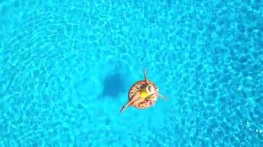 Havuzdaki bir çöreğin üzerinde sarı mayo giymiş bir kadının havadan görünüşü. Yaz yaşam tarzı, dinlenme ve rahatlama kavramı