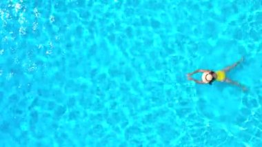 Havuzda yüzen sarı mayo giymiş bir kadının hava görüntüsü. Yaz yaşam tarzı